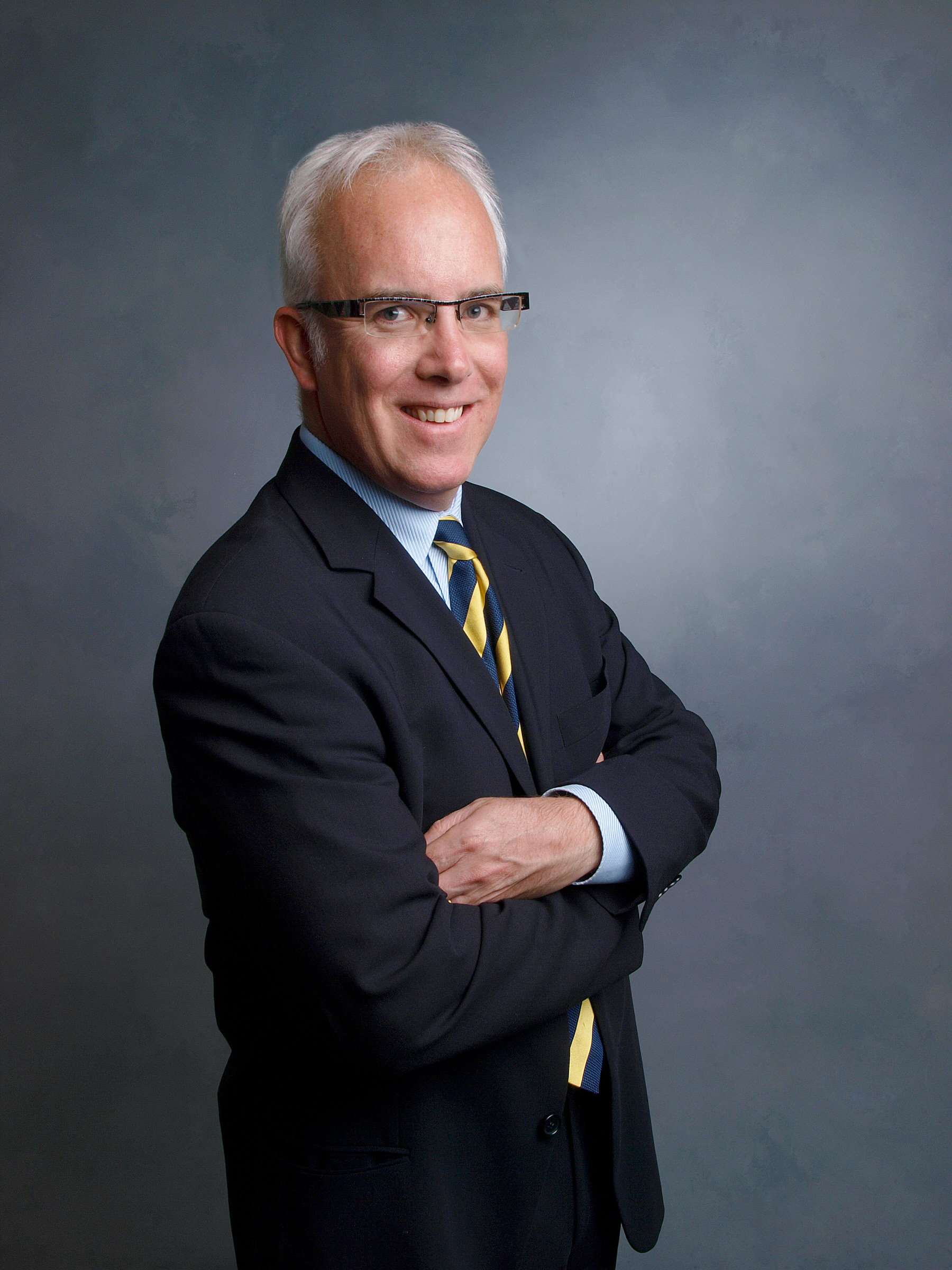 Photo of James McLeod, a middle-aged white man, with white hair wearing glasses, standing with his arms crossed with a friendly expression on his face.